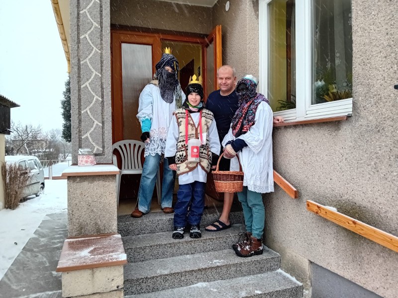 Tři králové v tradičních kostýmech stojí vedle občana obce, všichni se usmívají.